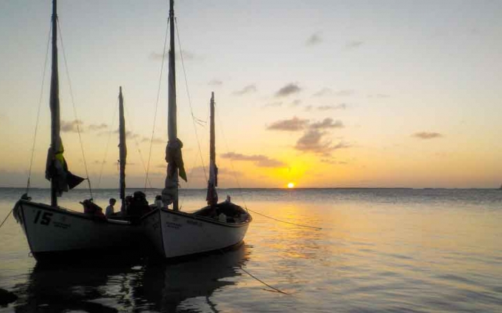 two sailboats rest on calm water at sunset